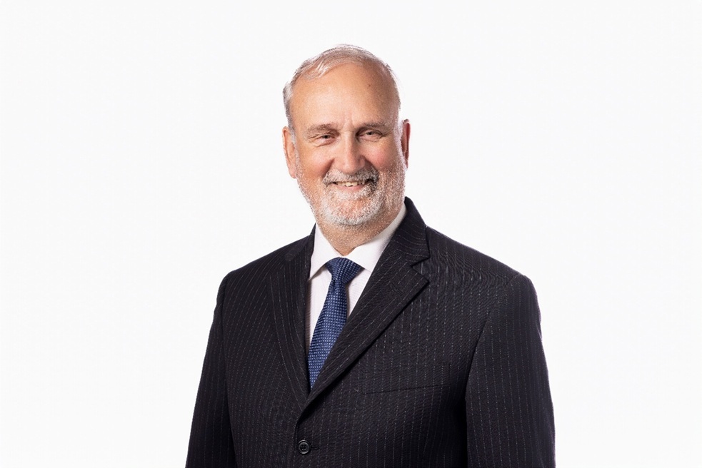 Smiling older man in a dark pinstripe suit and blue tie, posing for a professional headshot against a white background.